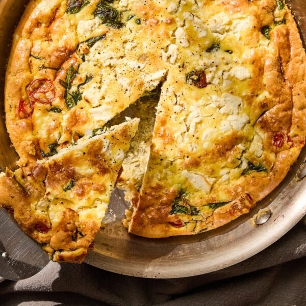 Skillet with wedge of tomato and spinach frittata being lifted.