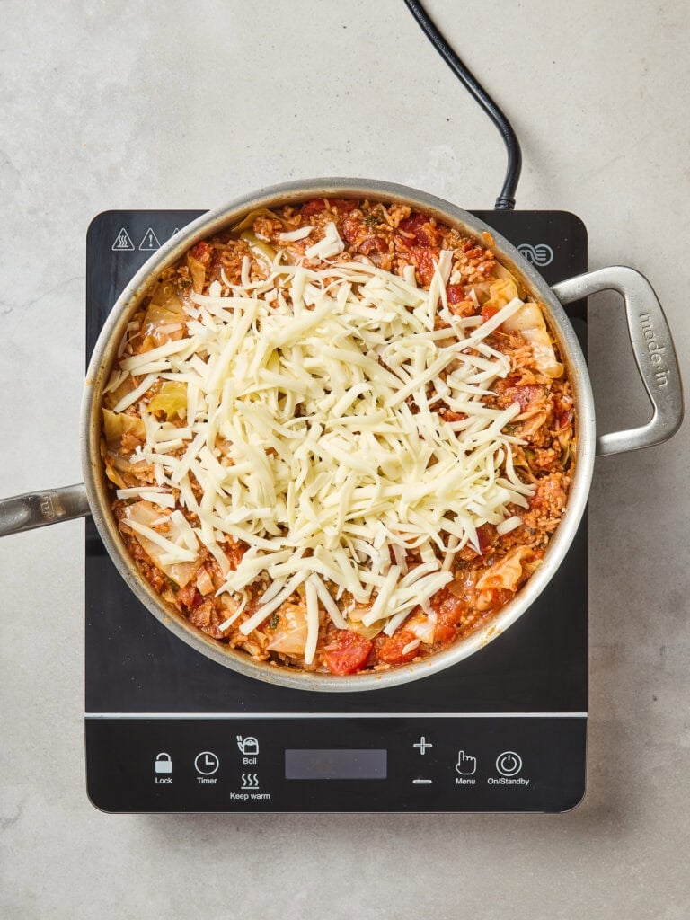 Shredded mozzarella cheese overtop a cabbage roll dish over heat.