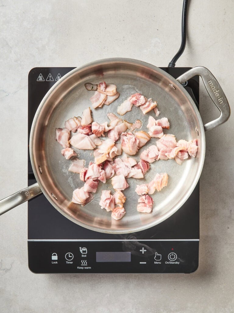 Bacon begins to cook in a skillet.