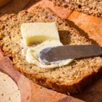 A pad of butter getting spread over a slice of banana bread.