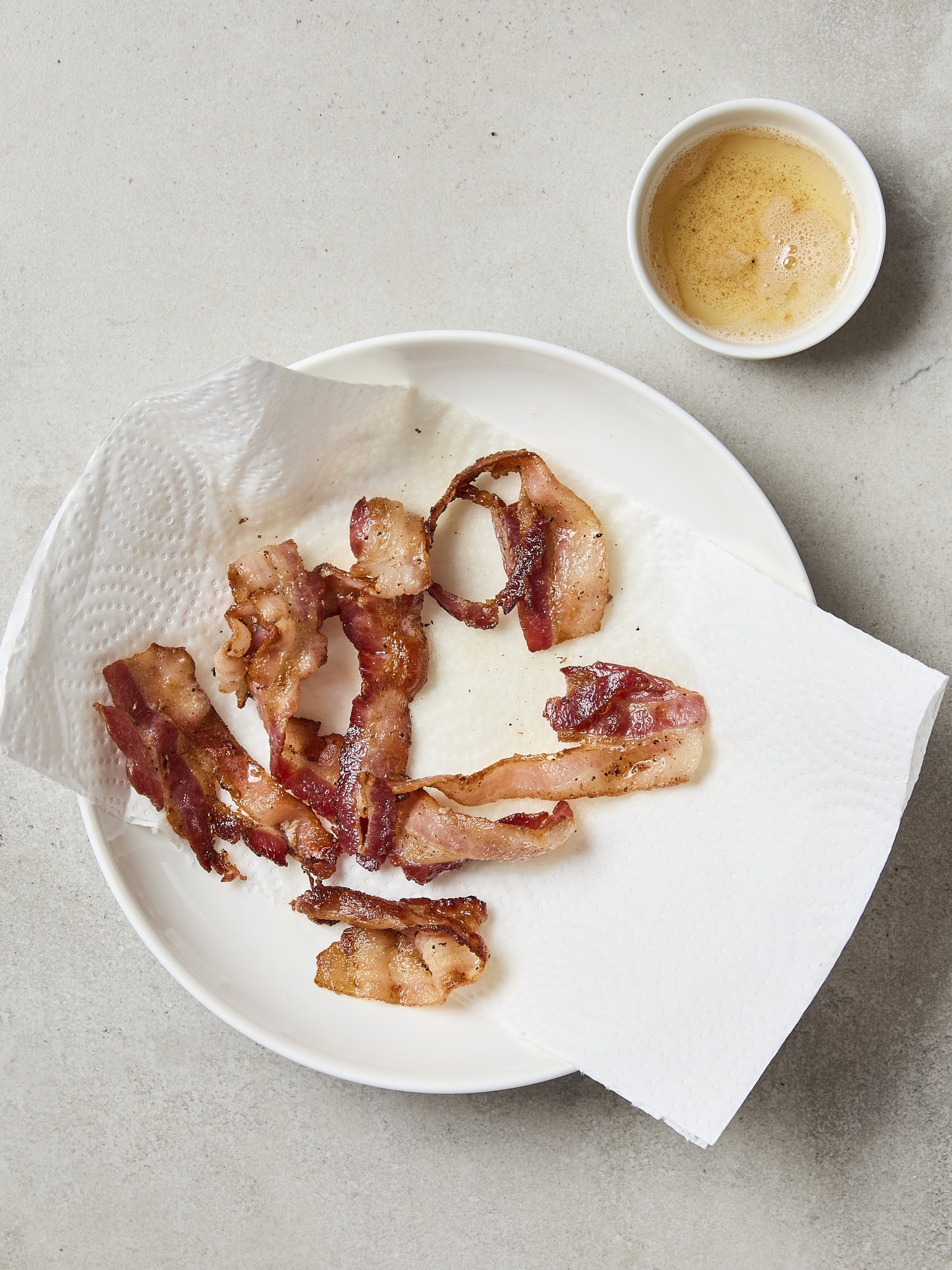 Cooked bacon on paper towel with bacon grease to side.