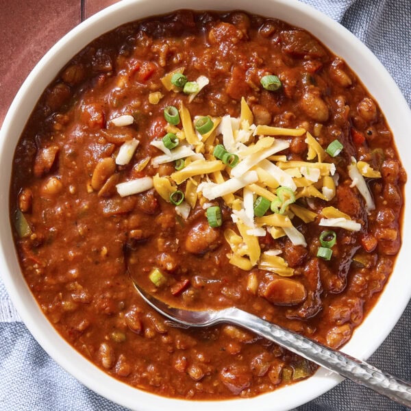 Bowl of chili with beans, cheese, scallions, and a spoon.