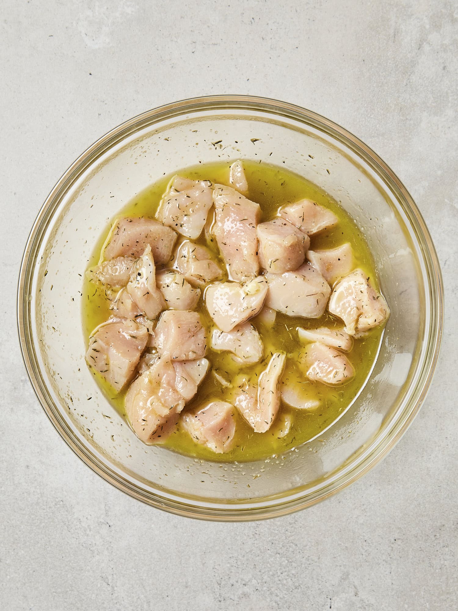 Glass bowl with marinated cubed raw chicken.