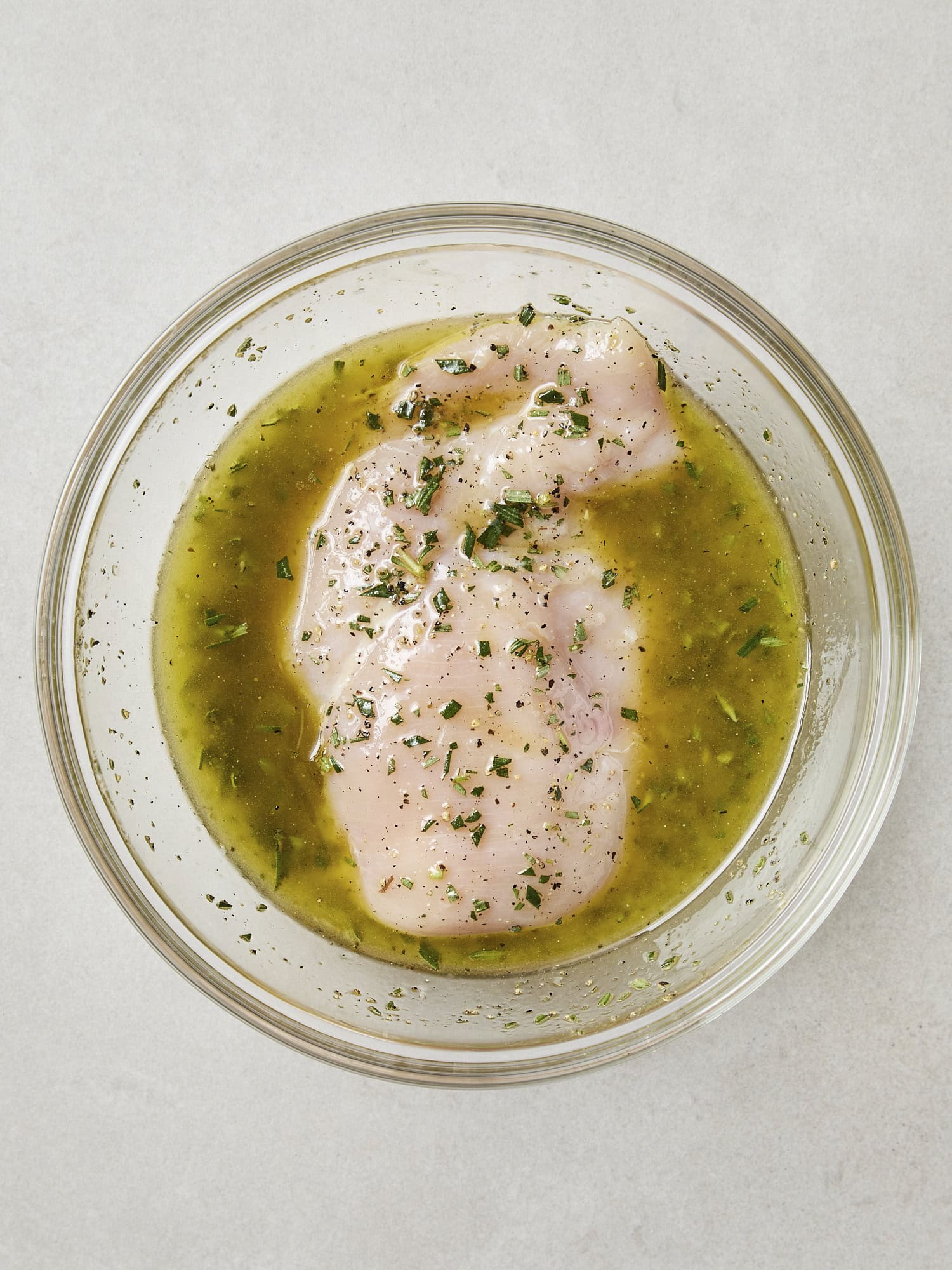 Chicken breast marinating in glass bowl.