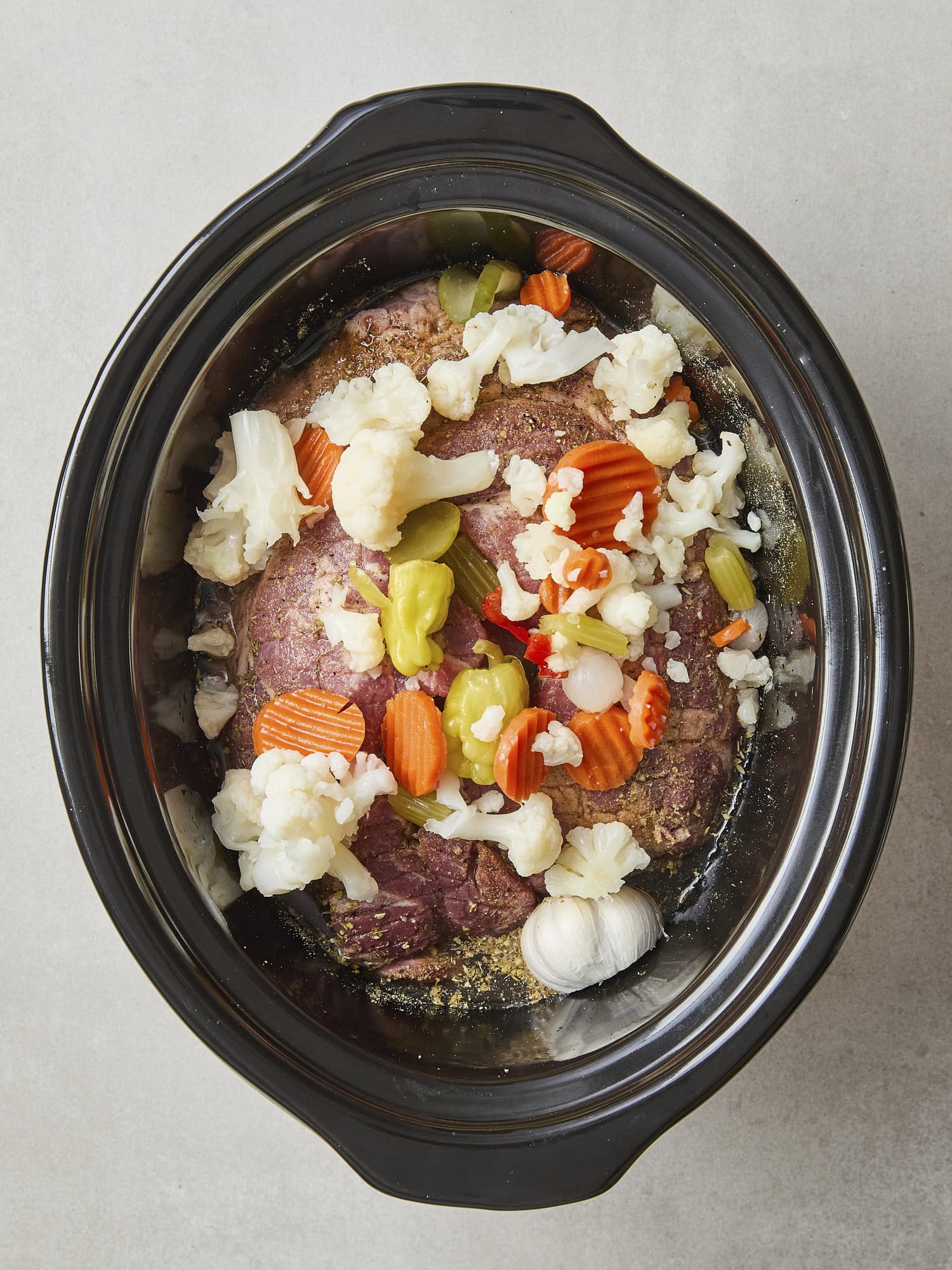 Pork shoulder in slow cooker with giardiniera on top.