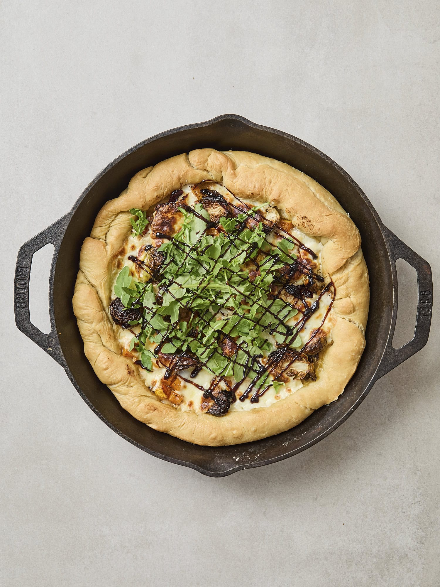 Butternut squash pizza with arugula and balsamic glaze drizzled on top.