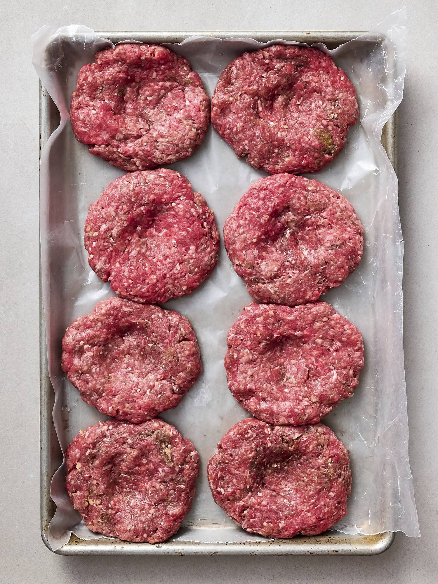 Burger patties with intent on a parchment-lined baking sheet.