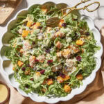 White bowl with butternut squash salad topped with cranberries, Parmesan, and walnuts.