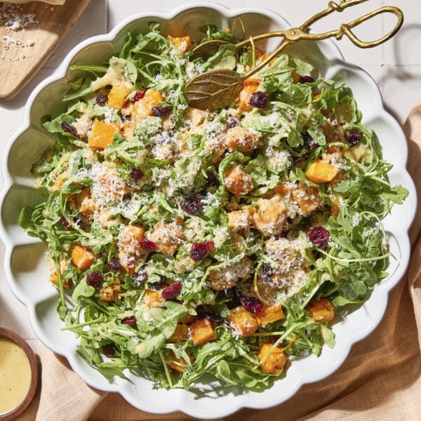 White bowl with butternut squash salad topped with cranberries, Parmesan, and walnuts.