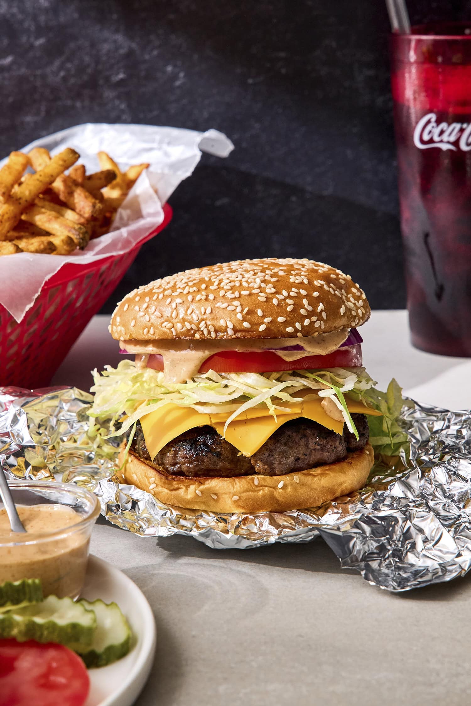 Grilled burger on bun with lettuce, cheese, tomato, and fries in background.