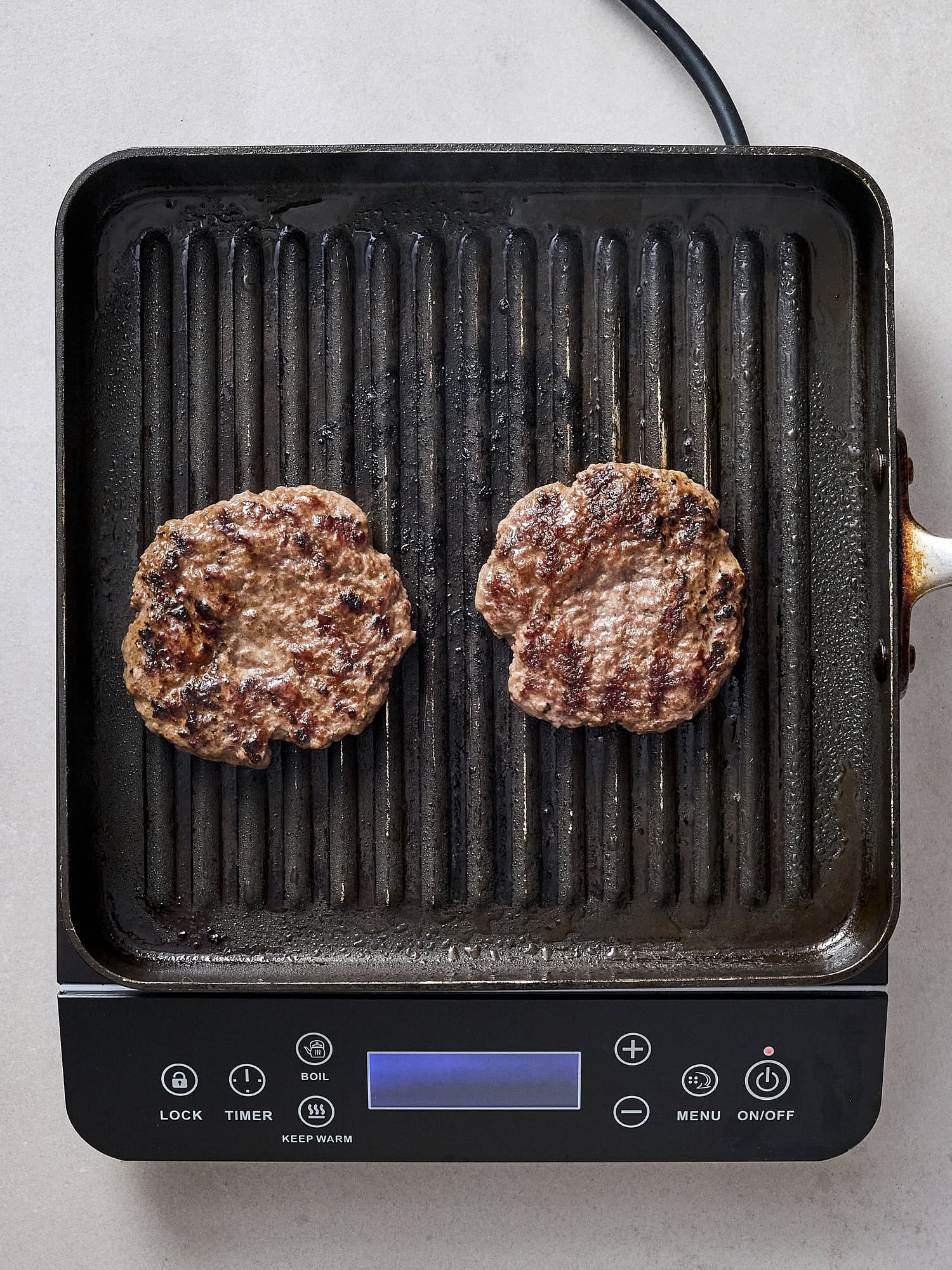 Cooked burger patties on grill with char.