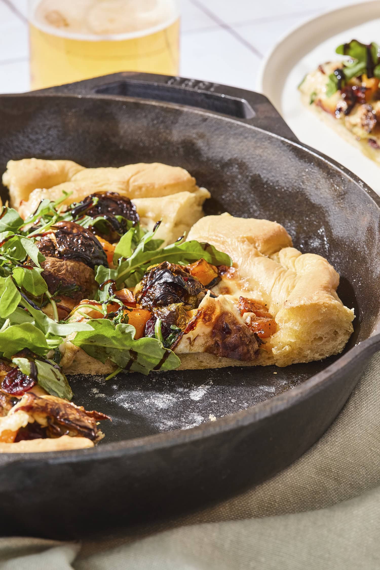 Slices cut of squash pizza with arugula and balsamic glaze on top.