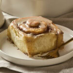 Cinnamon roll on plate with brown butter icing on top.