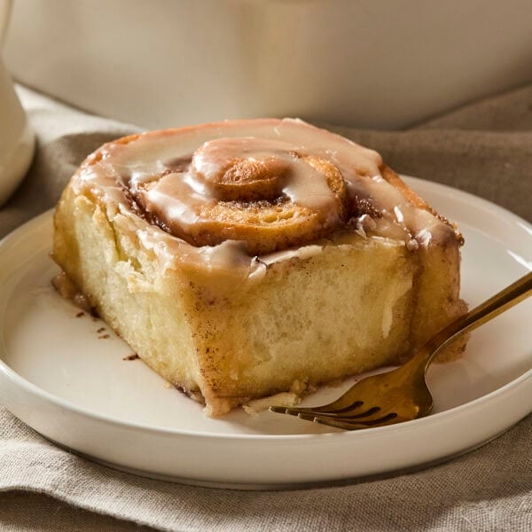 Cinnamon roll on plate with brown butter icing on top.