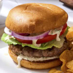 Grilled pork burgers with bun topped with homemade herb sauce.