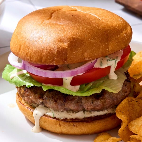 Grilled pork burgers with bun topped with homemade herb sauce.