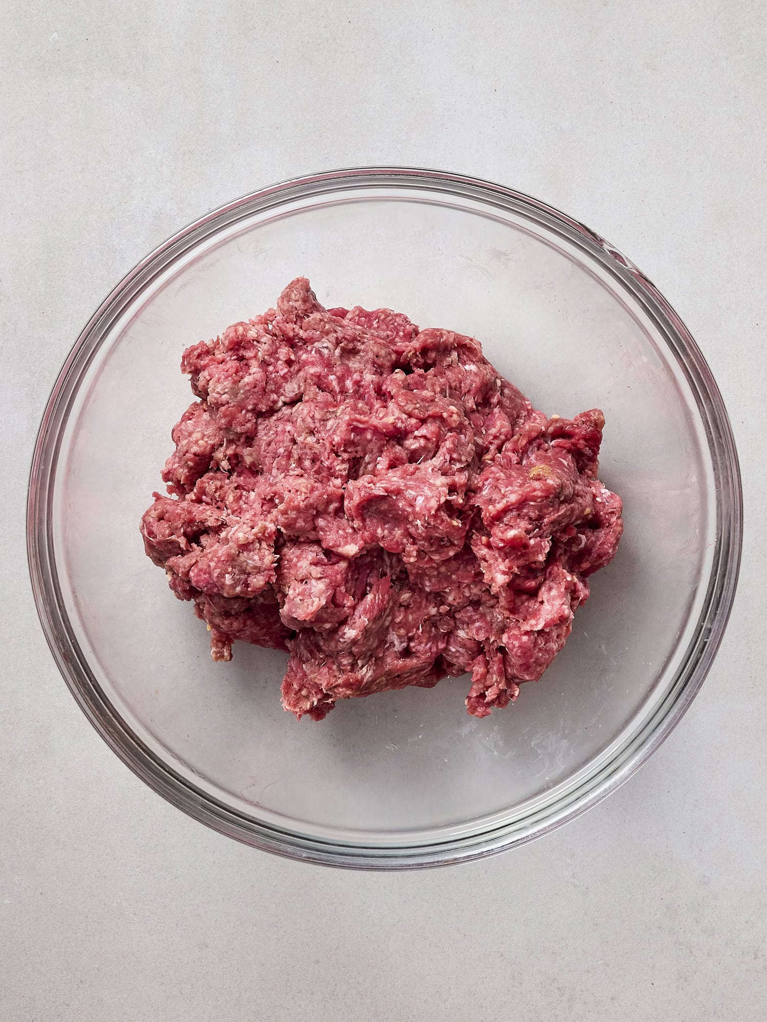 Glass bowl with ground beef mixture for grilled burgers.