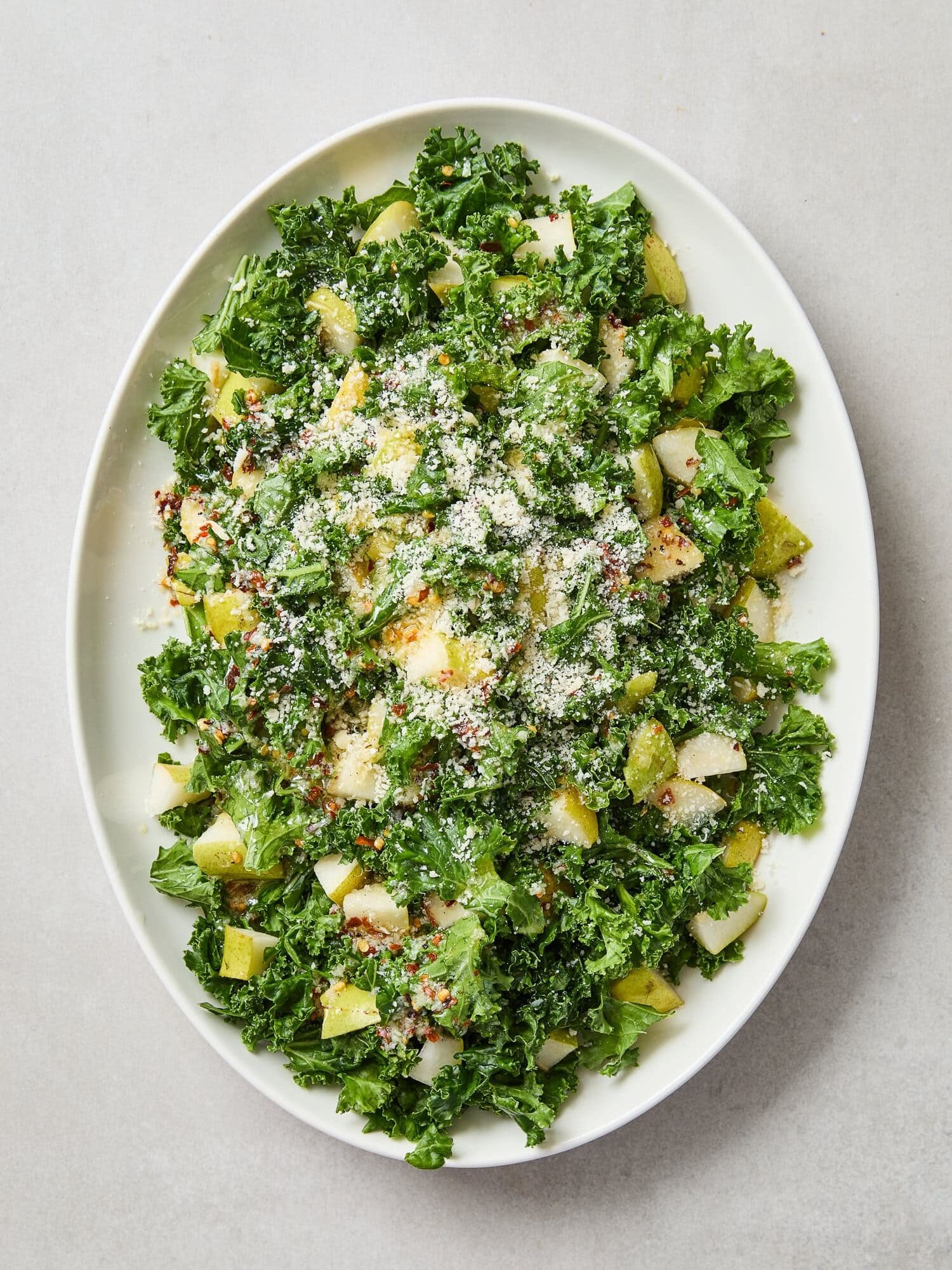 Spicy pear kale salad topped with Parmesan on a serving platter.