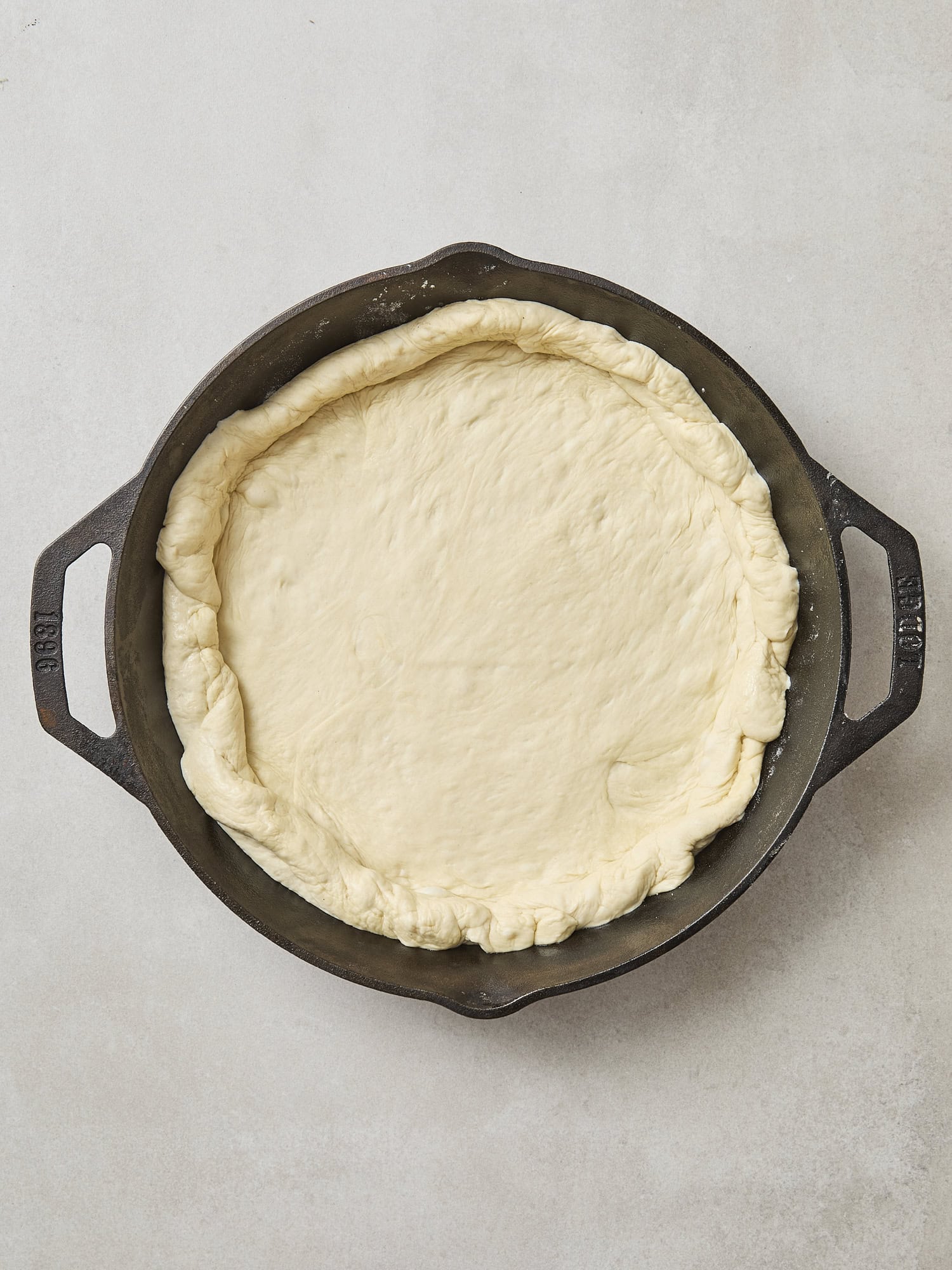 Cast iron skillet with unbaked dough inside for pizza.