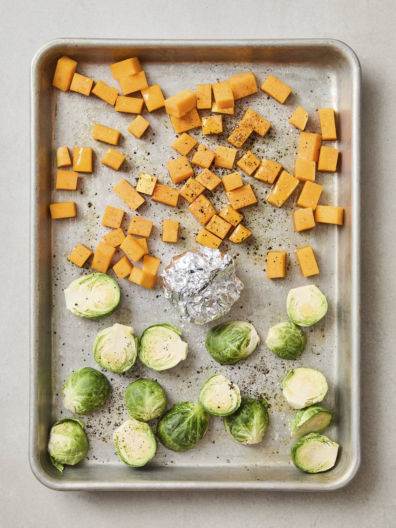 Butternut squash, garlic, and Brussels sprouts on roasting pan before going in oven.