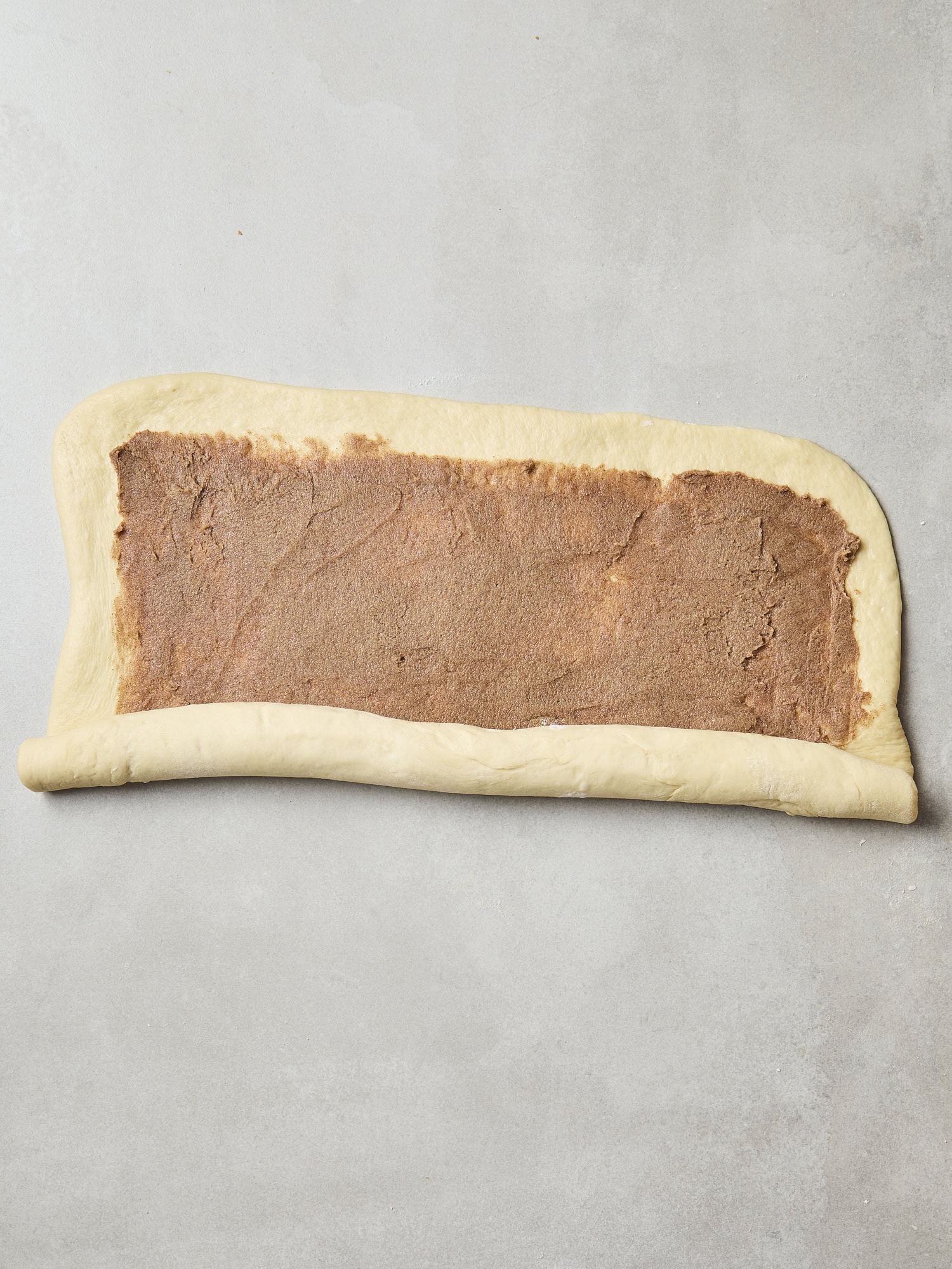 Cinnamon roll dough being rolled up into a log.