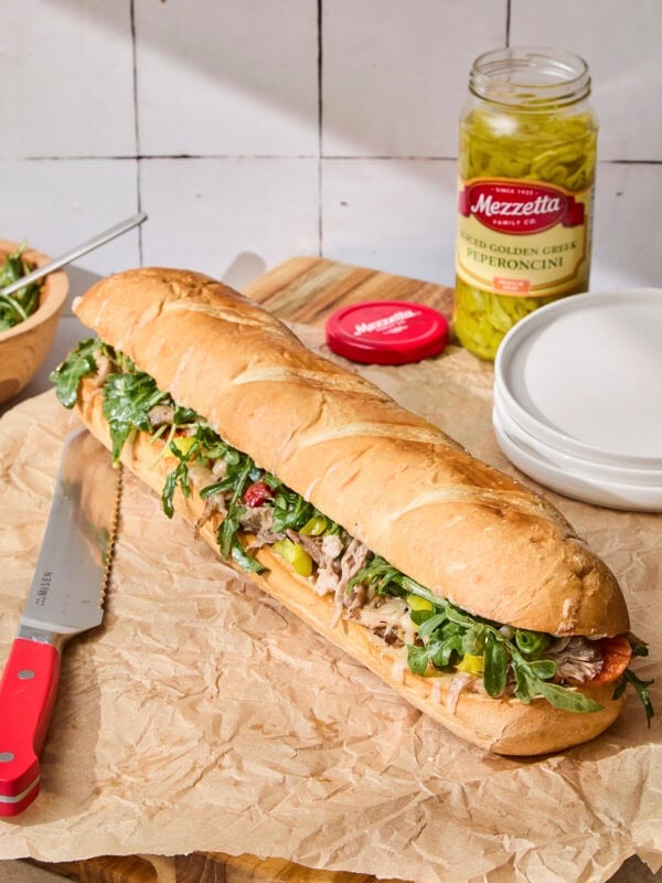 Italian pork sandwich with greens on top and plates in background.