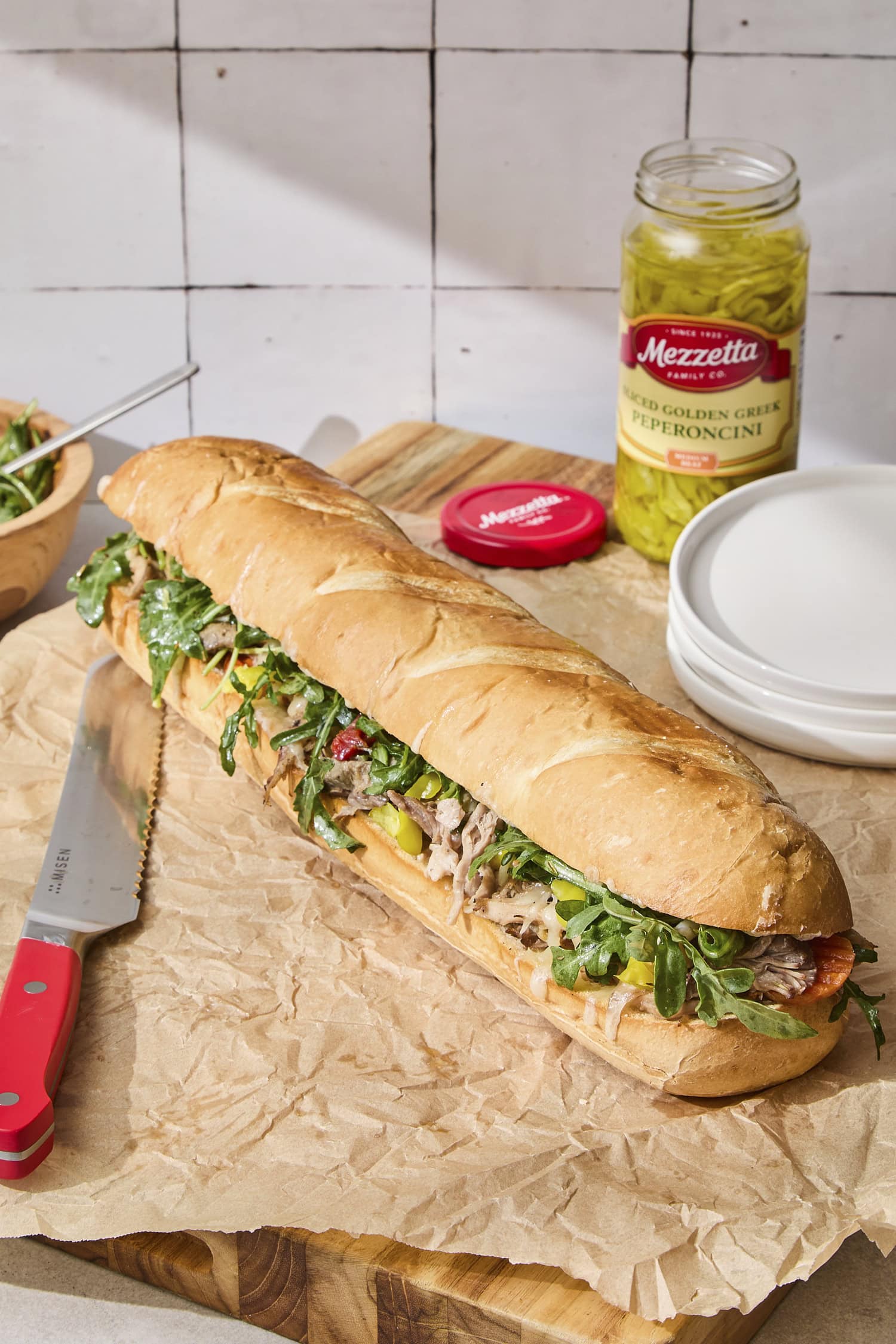 Italian pork sandwich with greens on top and plates in background.