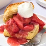 Strawberry rhubarb shortcake with whipped cream and biscuits on plate.
