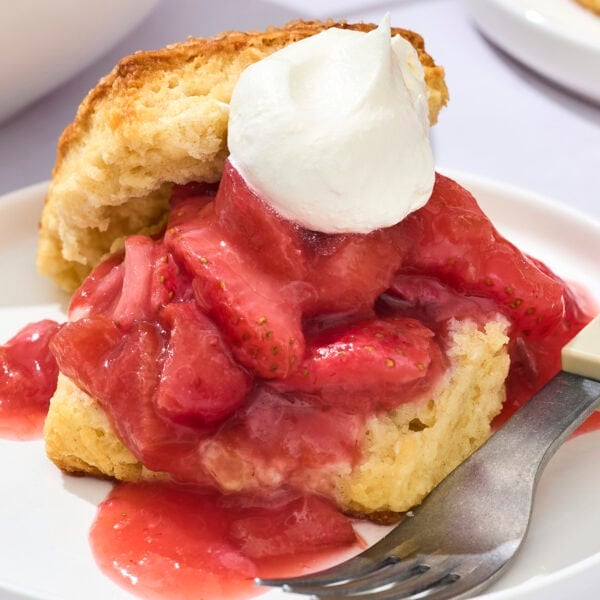 Strawberry rhubarb shortcake with whipped cream and biscuits on plate.