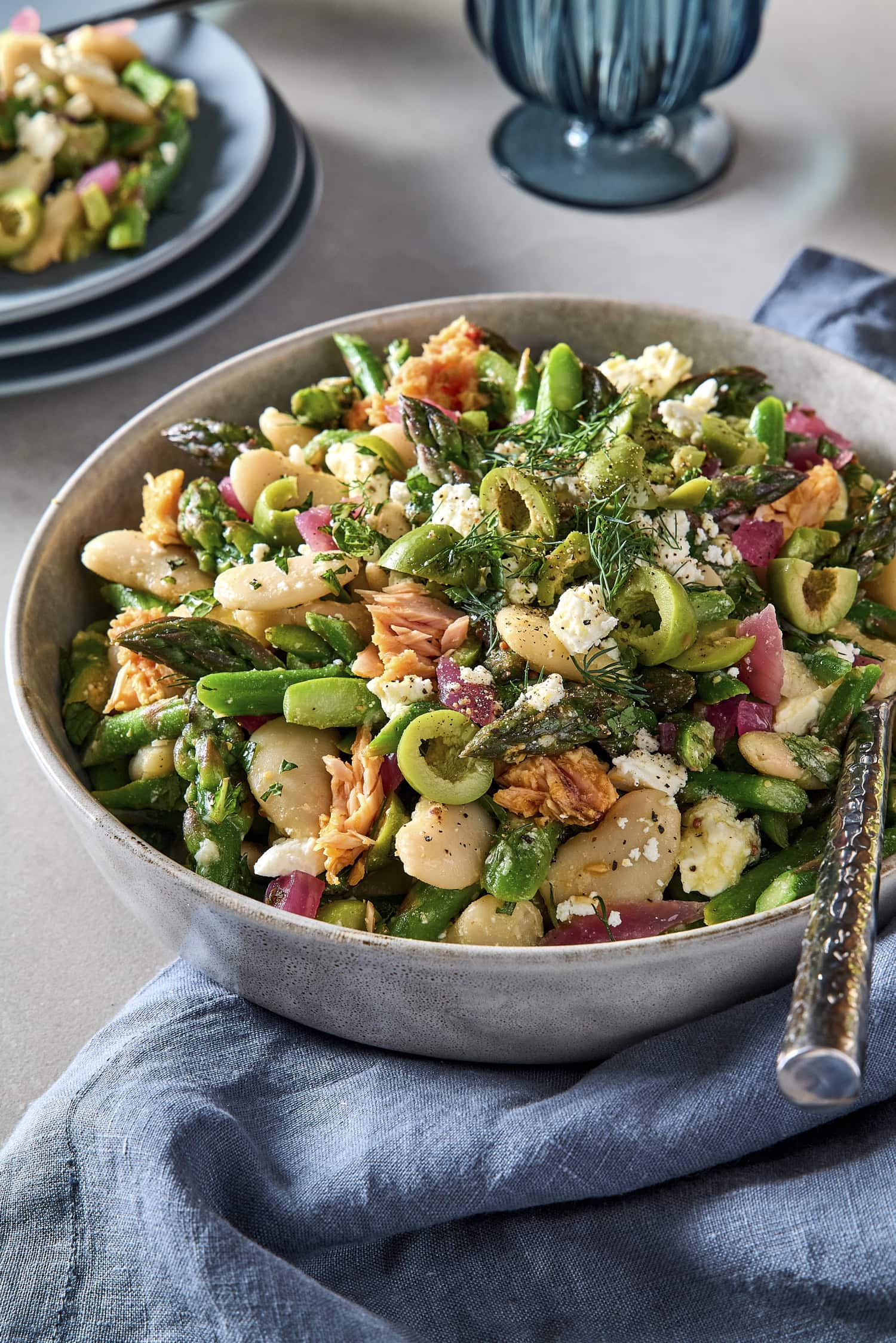 Bowl with asparagus spring salad topped with olives, feta, dill, and tuna.