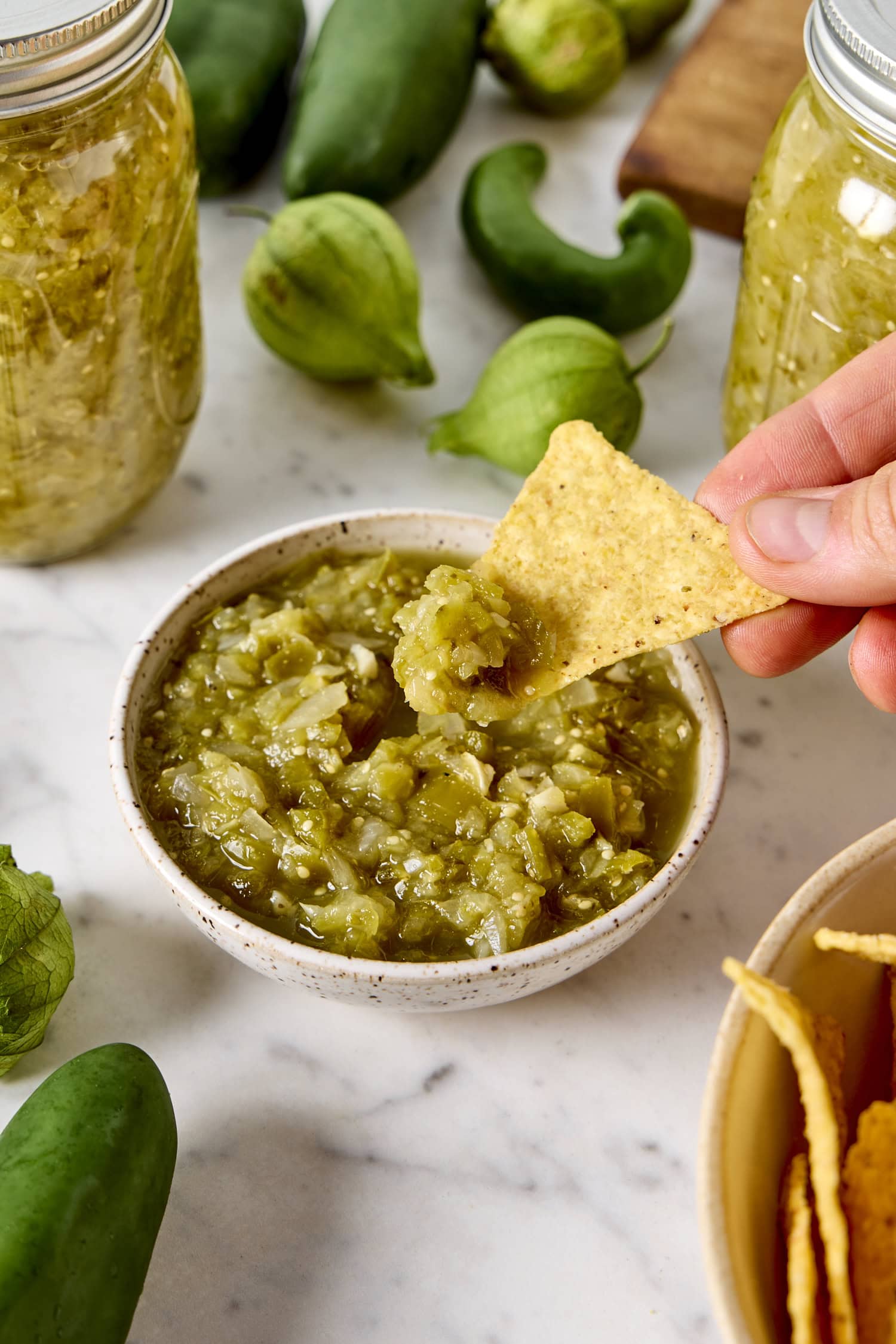 Tortilla chip scooping up some salsa verde from bowl.
