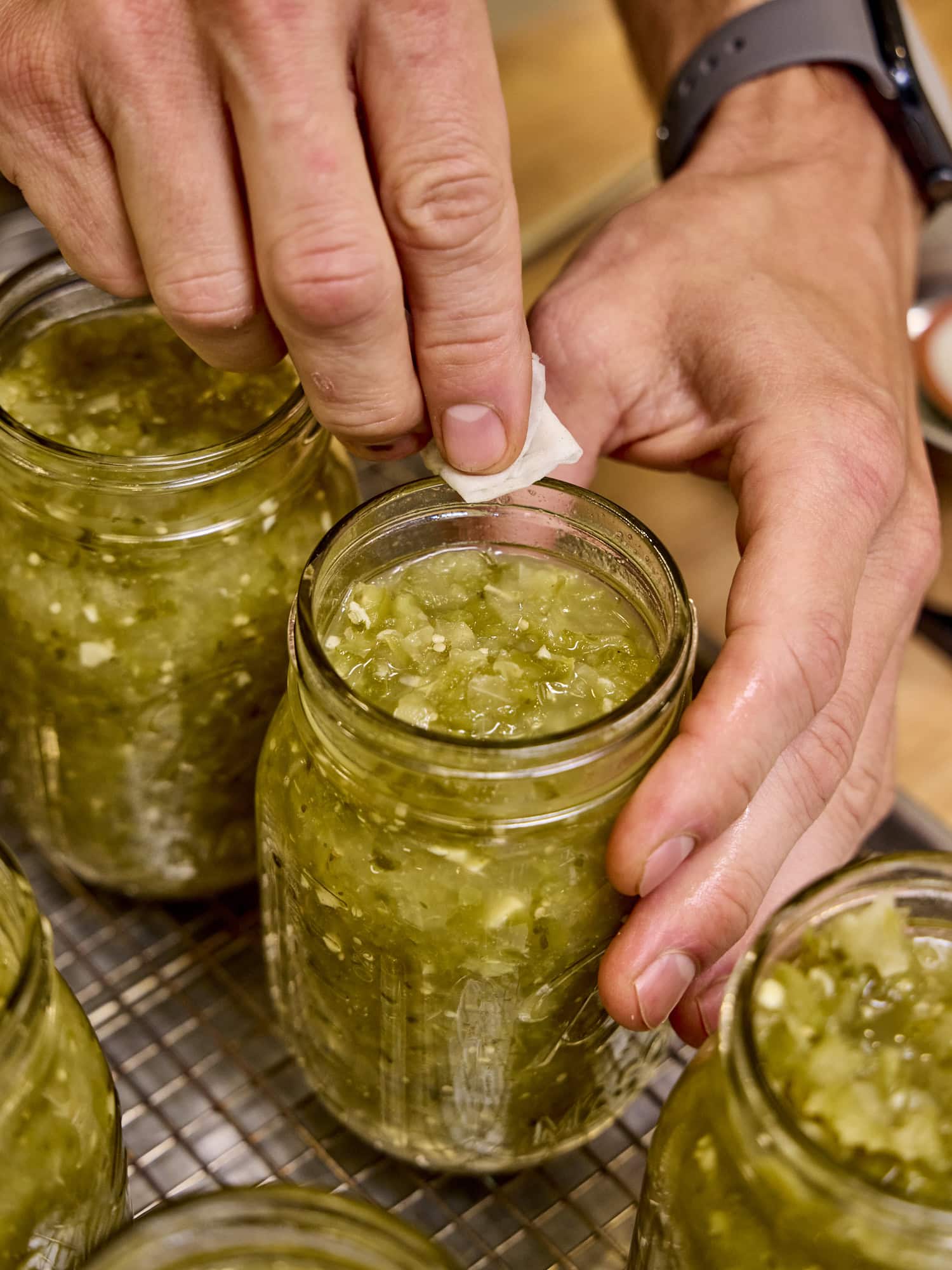 Wiping rim of jar filled with salsa verde made with tomatillos.