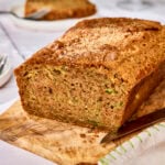 Loaf of zucchini bread on cutting board with slice removed.