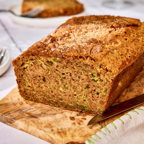 Loaf of zucchini bread on cutting board with slice removed.
