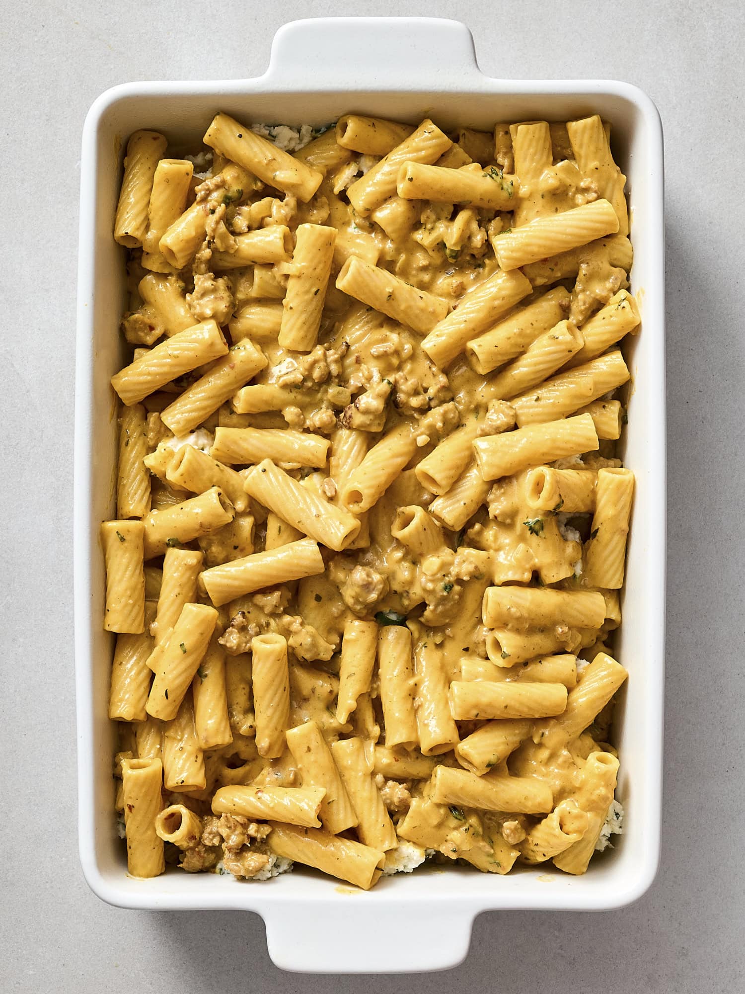 Baking dish with pasta mixed with a pumpkin sausage sauce.