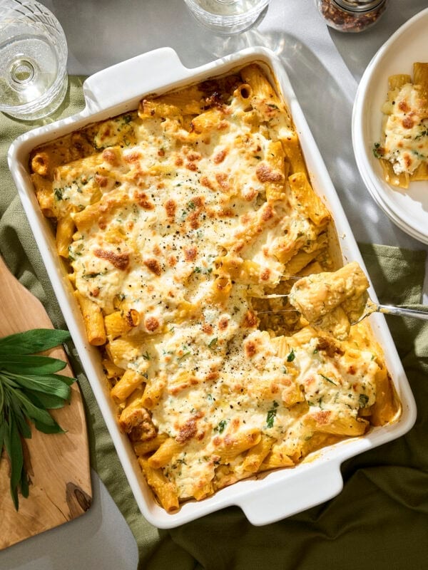 Spoon pulling out a serving of pumpkin baked ziti from casserole dish.