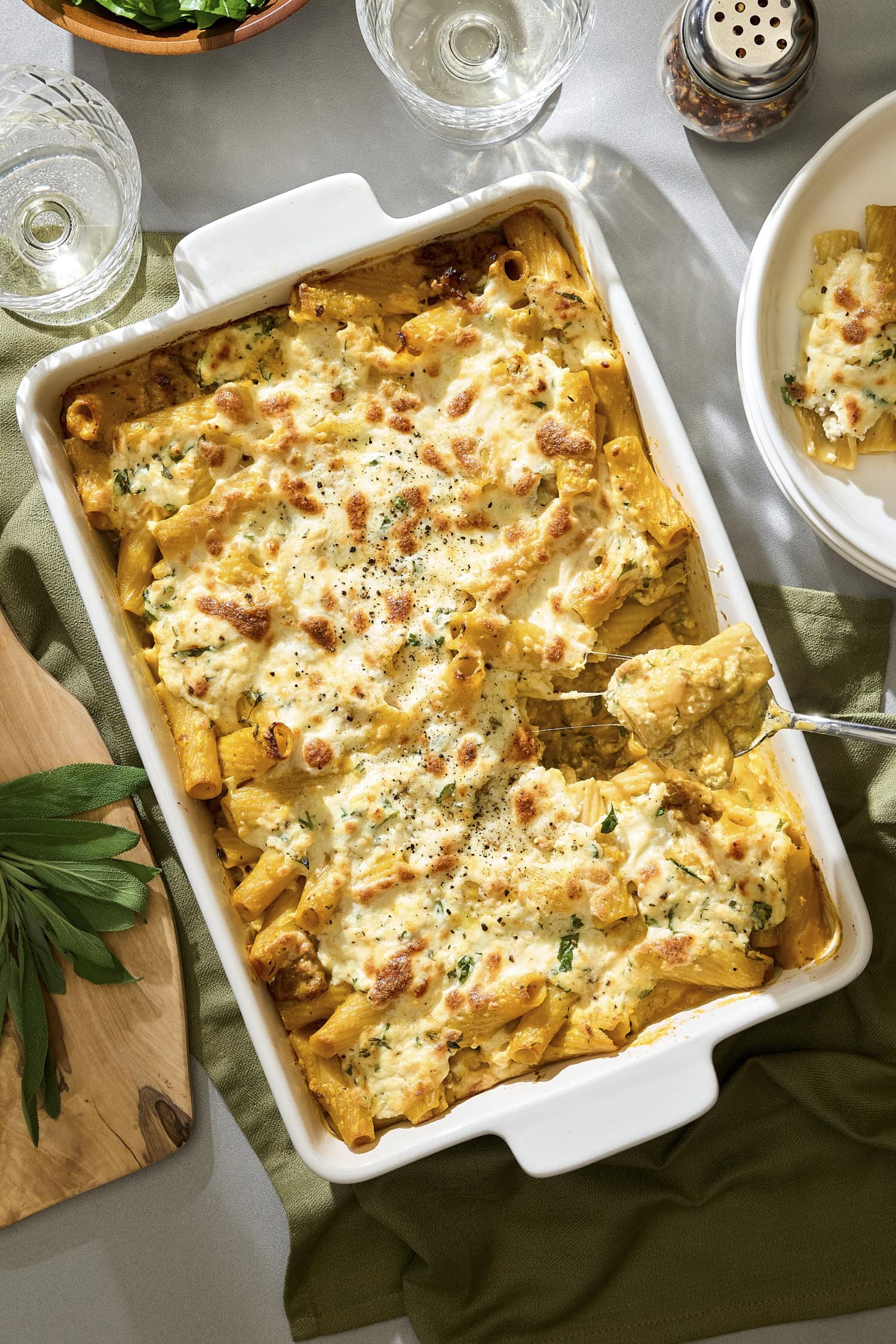 Spoon pulling out a serving of pumpkin baked ziti from casserole dish.