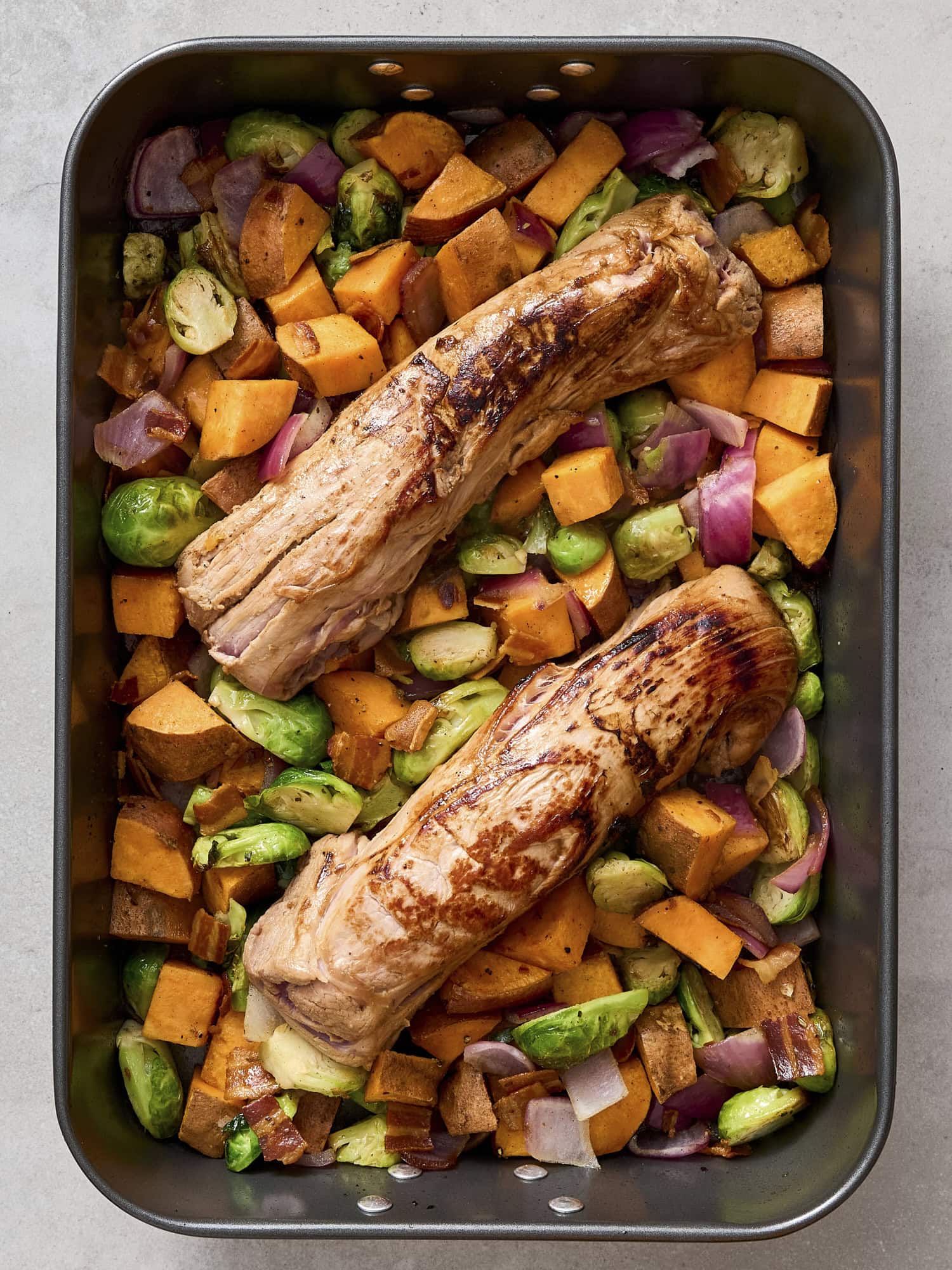 Pork tenderloins nestled on top of roasted vegetables in pan.