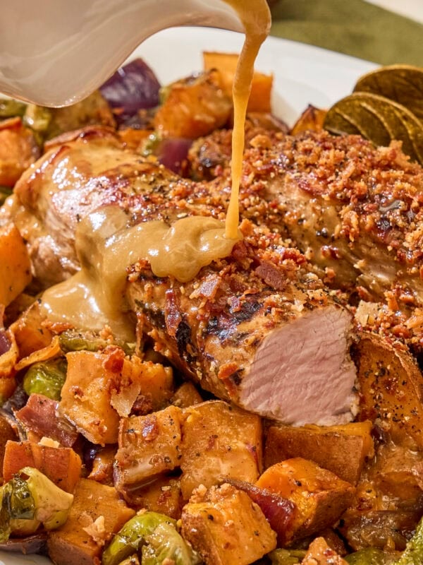 Sauce pouring on top of pork tenderloin with roasted vegetables underneath.