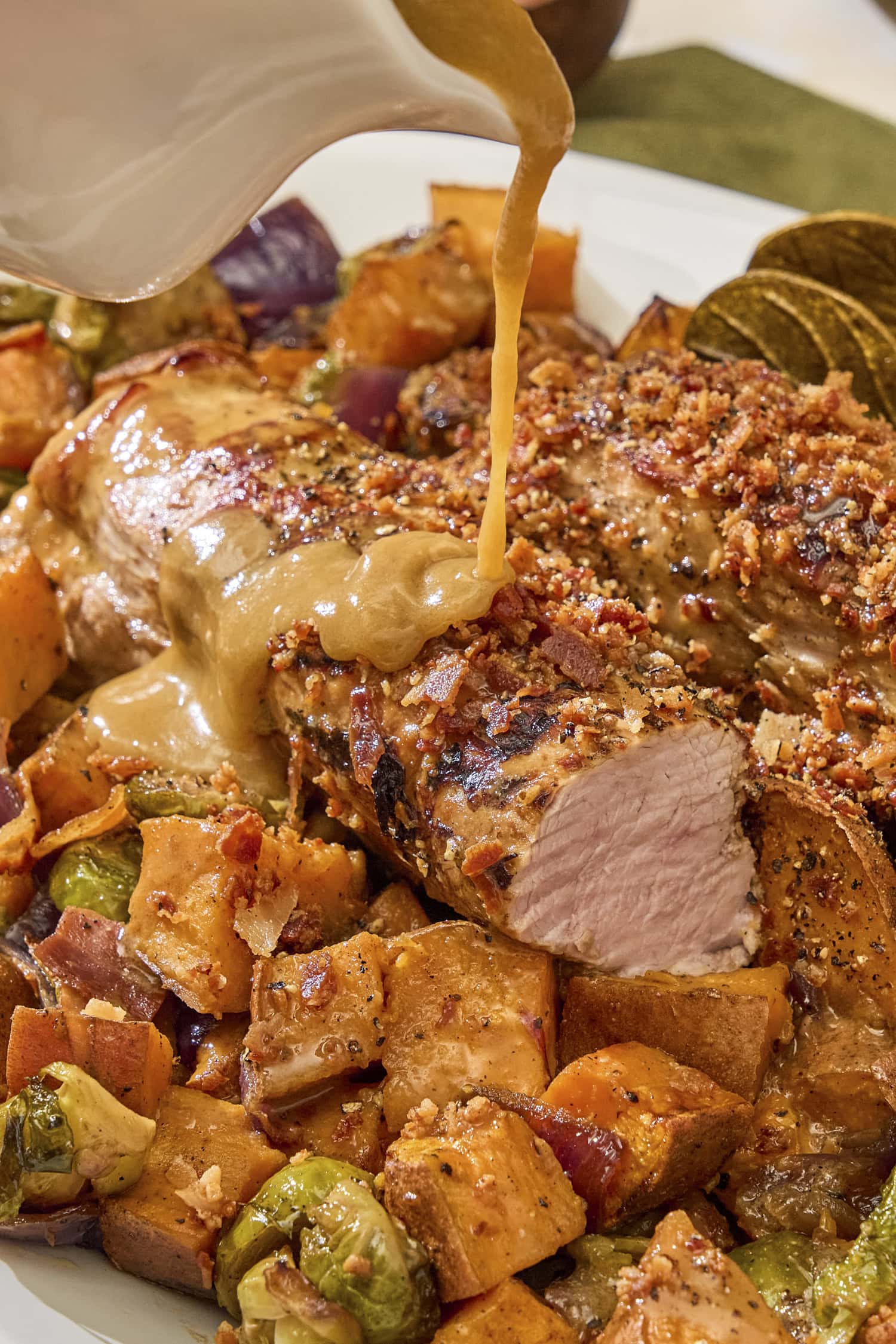 Sauce pouring on top of pork tenderloin with roasted vegetables underneath.