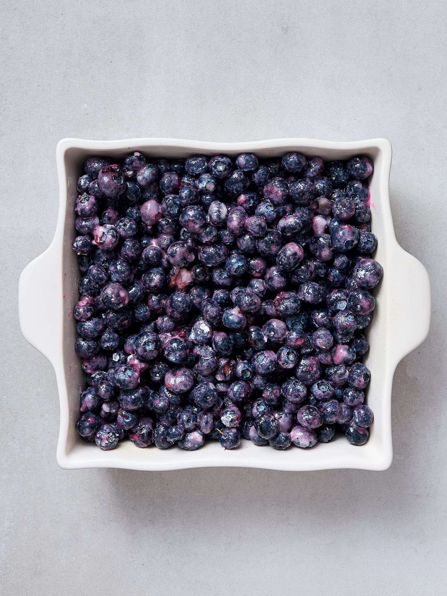 Partially mashed blueberries in a baking dish for a blueberry crumble.