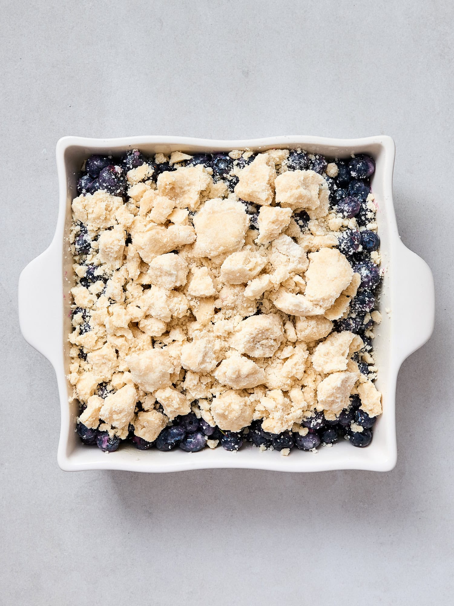 Blueberries with a crumble topping in a dish prior to baking.