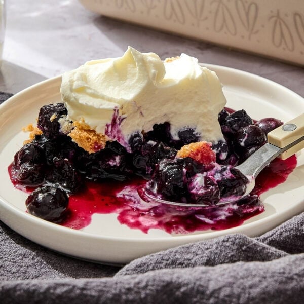 Blueberry crumble topped with whipped cream on a plate.
