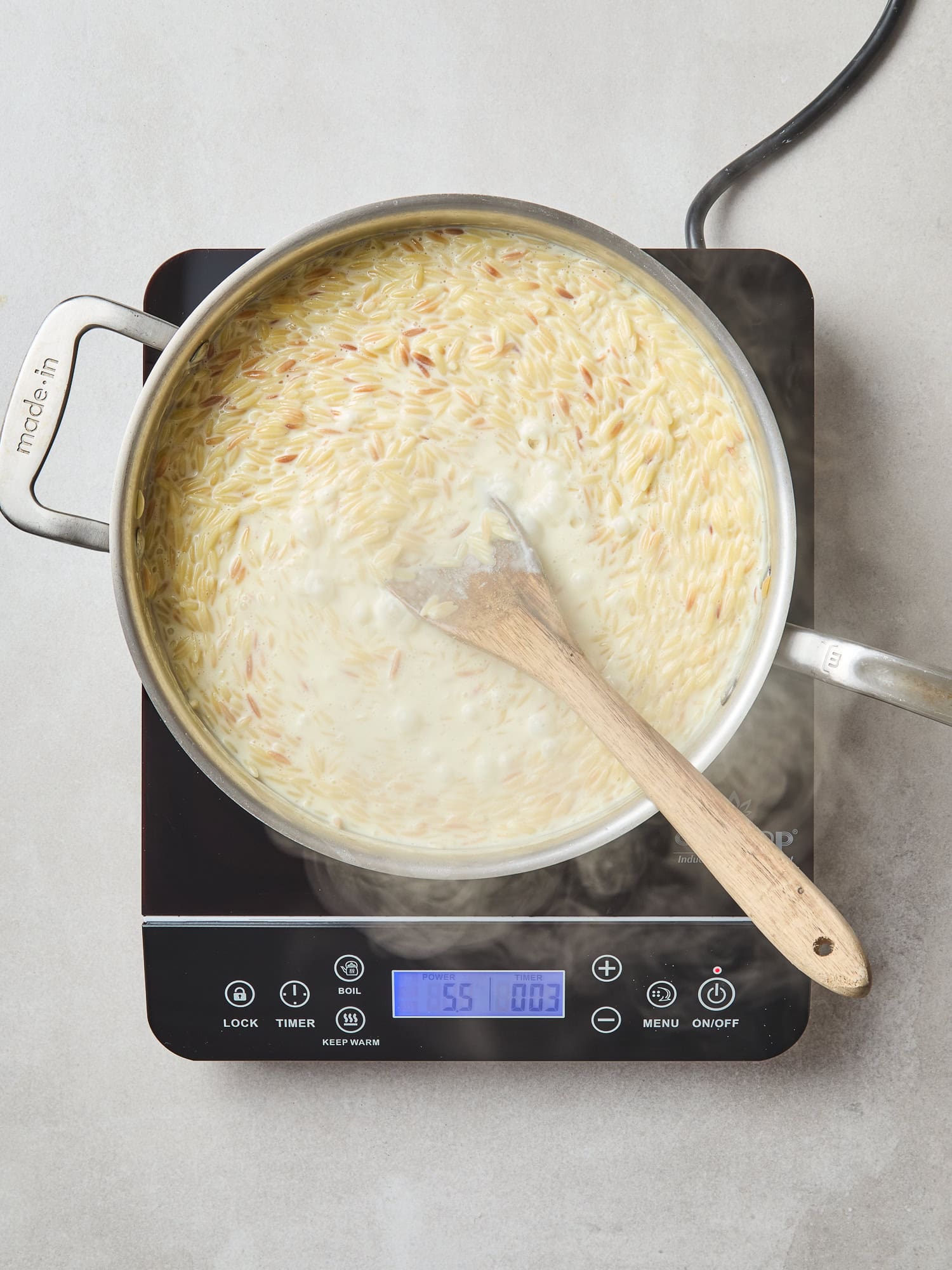 Orzo thickening with cream and Parmesan cheese in a skillet.