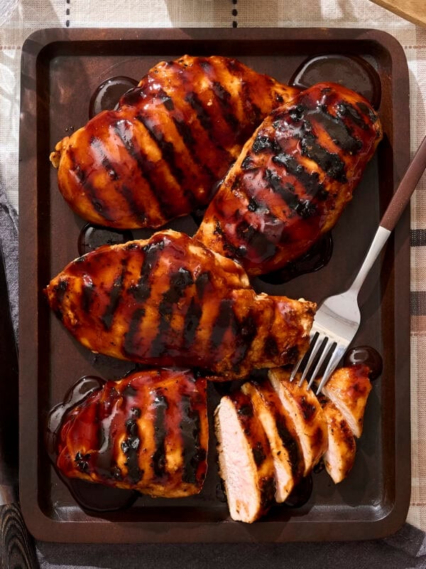 Platter of BBQ sauce-covered grilled chicken with slices.