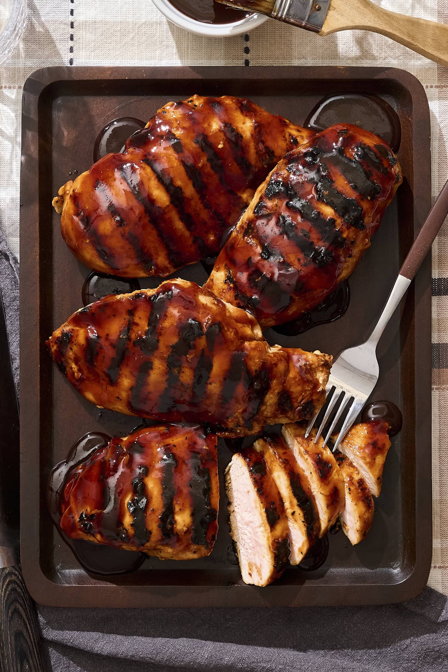 Platter of BBQ sauce-covered grilled chicken with slices.