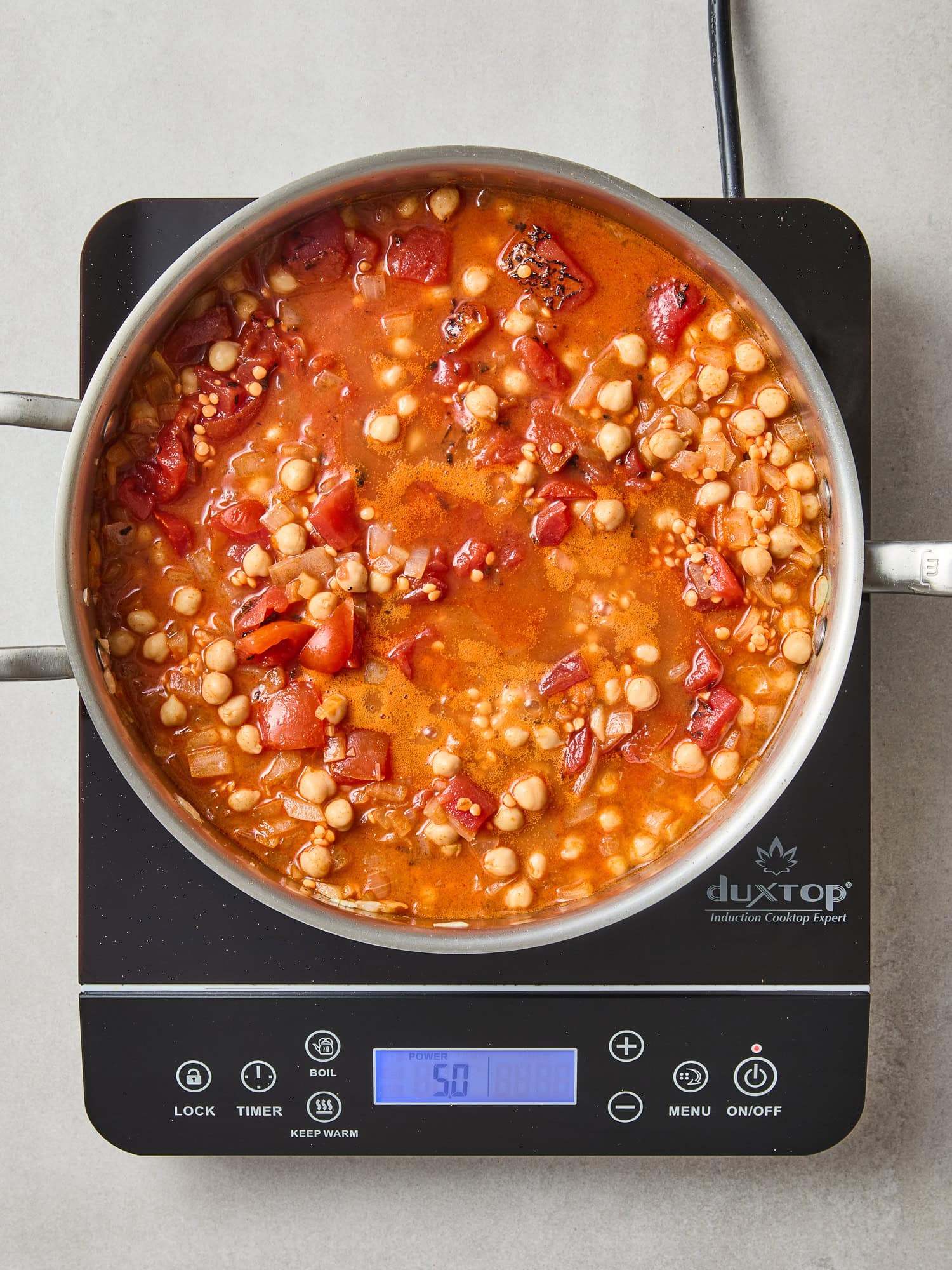 Chickpeas and red lentils simmer over heat with tomatoes.