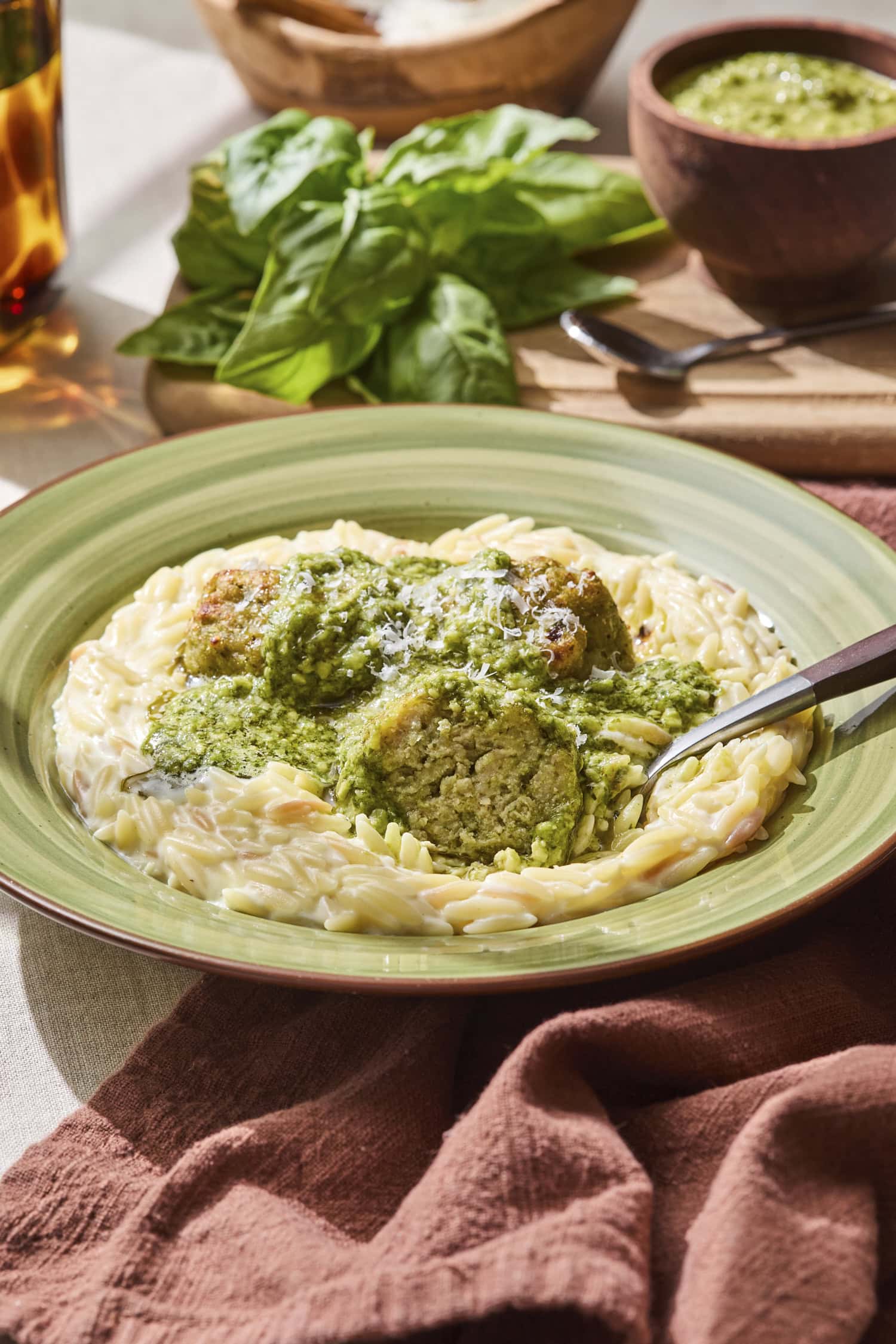 A bowl full of orzo with chicken meatballs topped with pesto and Parmesan cheese.