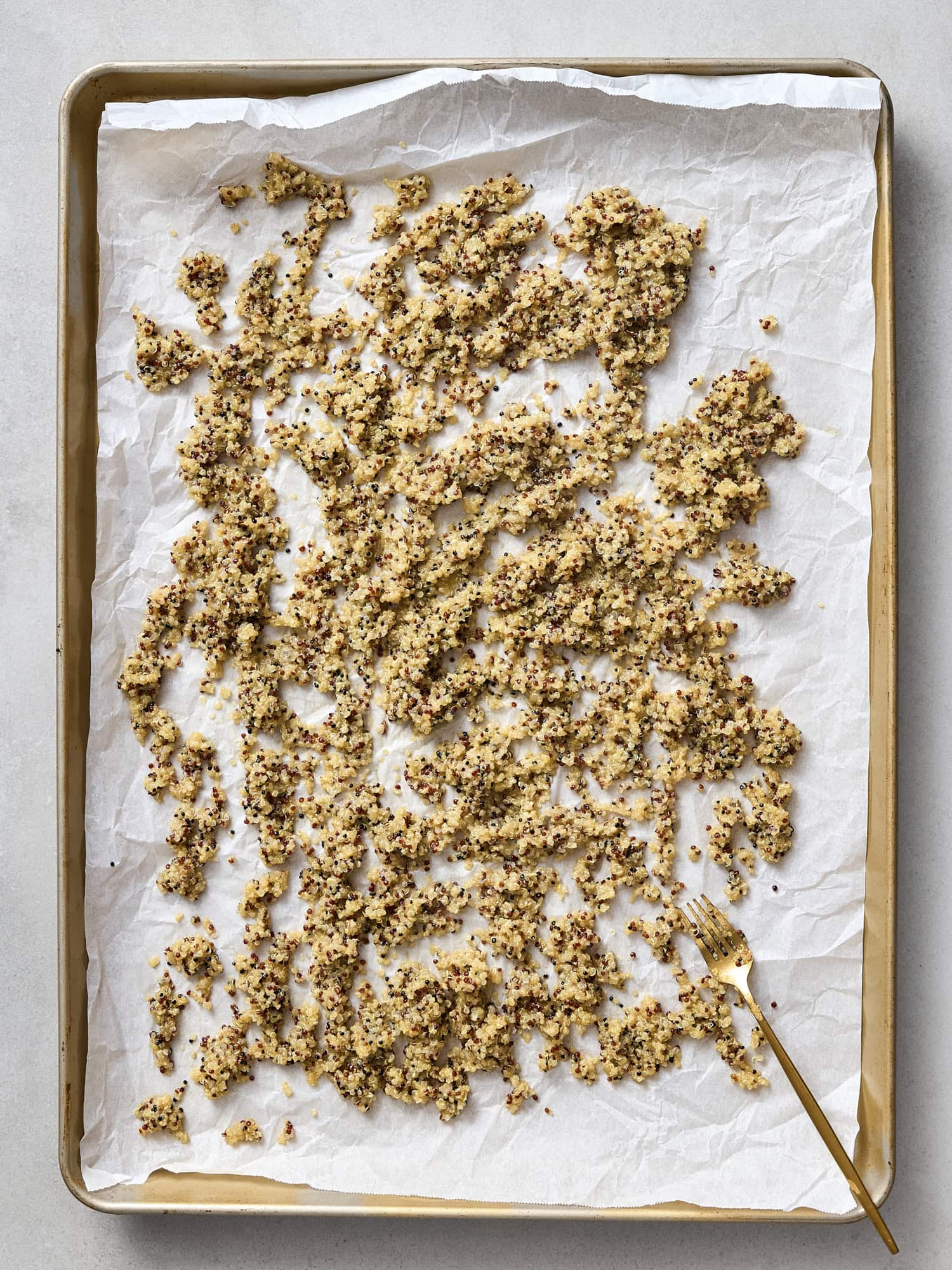 Cooked quinoa spread on sheet pan to bake.