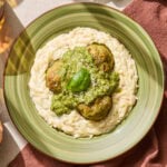 A bowl full of orzo topped with chicken meatballs coated in pesto and Parmesan cheese.